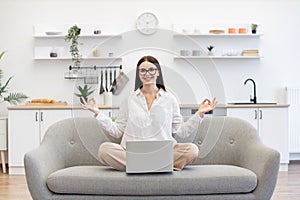 Woman sitting on couch with wireless laptop in front of her and meditating.