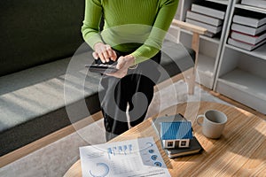 woman sitting on cozy sofa and planning and calculate expense and mortgage with calculator and home on desk, insurance