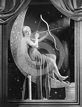 Woman sitting on crescent moon with bow and arrow