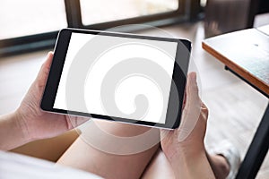 A woman sitting cross legged and holding black tablet pc with blank white desktop screen