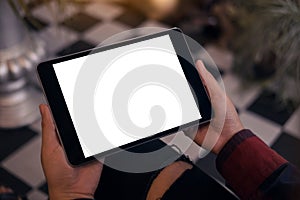 A woman sitting cross legged and holding black tablet pc with blank white desktop screen in cafe