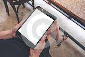 A woman sitting cross legged and holding black tablet pc with blank white desktop screen in cafe