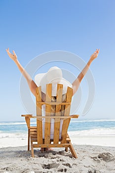 Woman sitting in deck chair at the beach with arms up