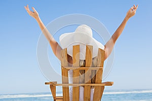 Woman sitting in deck chair at the beach with arms up