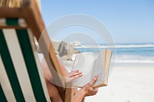 Woman sitting in deck chair at the beach reading