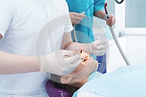 A woman is sitting in a dental chair at a dentist`s reception. A male doctor is treating the patient teeth.