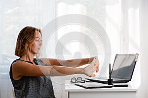 A woman sitting at a Desk doing a workout from fatigue. White window in the background. Copy space. The concept of fatigue at work