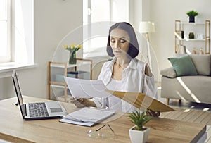 Woman sitting at desk in her home office and reading business letters and documents