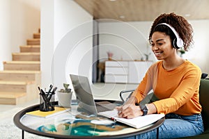 Woman sitting at desk, using computer and writing in notebook