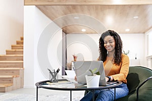 Woman sitting at desk, using computer and writing in notebook