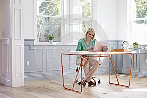 Woman Sitting At Desk Using Mobile Phone In Home Office