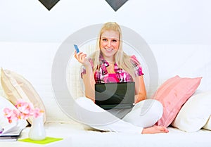 Woman sitting on divan with laptop and credit card