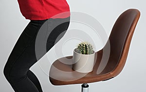 Woman sitting down onto chair with cactus against background, closeup. Hemorrhoids concept