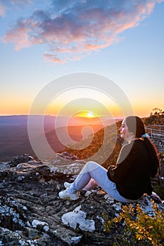 Woman sitting on edge of Reed Lookout cliff while enjoying sunset