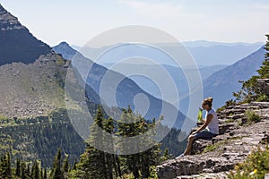 Woman sitting on the edge of scenic mountain overlook drinking water.