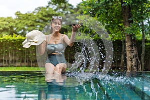 Woman sitting on edge of swimming pool and playing water splashing