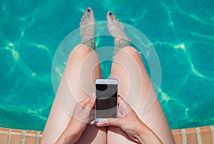 Woman sitting at the edge of swimming pool and using blank scree