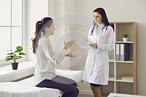 Woman sitting on examination bed and talking to doctor during medical consultation at clinic