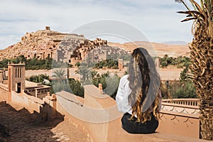 Woman sitting on fence with view of famous moroccan old town in Ouarzazate