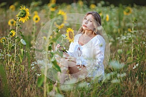 Woman sitting in the field among sunflowers.