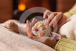 Woman sitting by the fireplace petting her cute ginger kitten