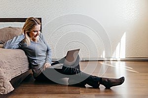 Woman sitting on the floor in bedroom and having Zoom video conference call via computer with friend.