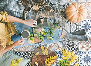 Woman sitting on floor with cat and drinking autumn tea