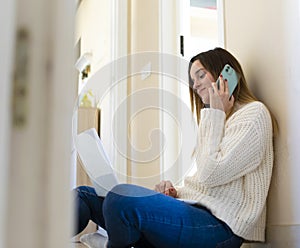 Woman sitting on the floor while teleworking from home and smiling while talking on the phone. Covid-19 work