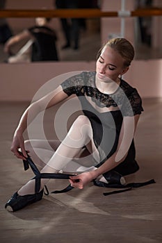 Woman sitting on the floor and tying ribbons on her pointe shoes. Vertical photo.