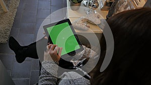 Woman sitting on the floor and using vertical tablet computer with green screen. Close up shot of woman`s hands with pad