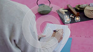 Woman sitting on floor, writing notes in diary during meditation