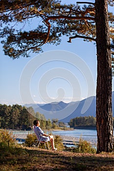 A woman is sitting on a folding chair on the bank of a mountain river