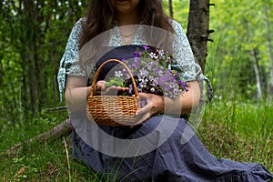 A woman is sitting in the forest on the grass with a bouquet of forest flowers.