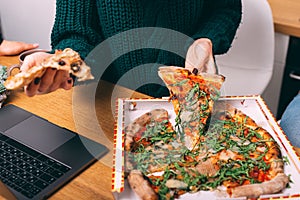 Woman sitting in front of laptop in office and having meal time during lunch time with hot tasty pizza