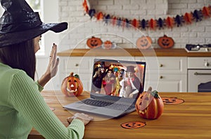 Woman sitting in front of laptop and waving hello to friends at virtual Halloween party photo