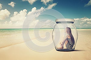 Woman sitting in a glass jar on a beach looking at the ocean view