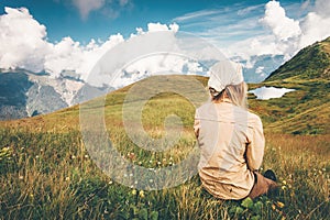 Woman sitting on grass valley enjoying mountains and lake