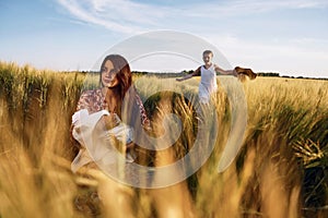 Woman is sitting on the ground. Mother with her newborn baby and girl is on the field at sunny day together