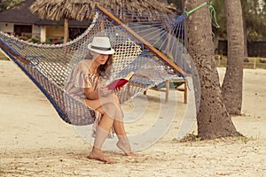 Woman sitting in a hammock on the beach reading a book