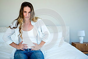 woman sitting on her bed gripping her stomach