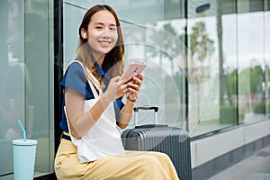woman sitting with her suitcase, using her mobile phone to send messages and stay connected