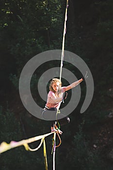 A woman is sitting on a highline, trying to get up