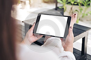 Woman sitting and holding black tablet pc with blank white desktop screen , feeling relaxed with sand and beach background