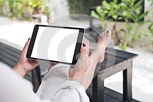 A woman sitting and holding black tablet pc with blank white desktop screen , feeling relaxed with sand and beach background