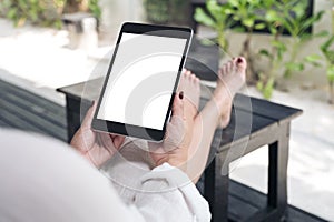 A woman sitting and holding black tablet pc with blank white desktop screen , feeling relaxed with sand and beach background