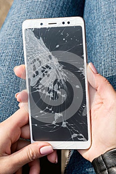 Woman is sitting and holding a broken smart phone with a cracked screen
