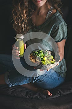 Woman sitting and holding healthy superbowl and smoothie