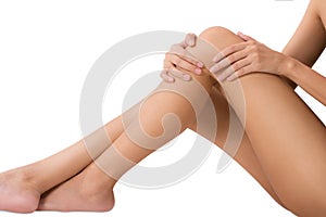 Woman sitting and holding her beautiful healthy long leg with massaging knee and thigh in pain area.