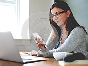 Woman sitting in home office checking mobile phone.