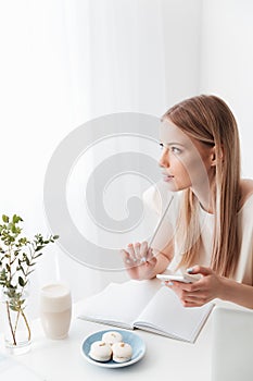 Woman sitting indoors near sweeties holding mobile phone.